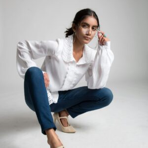 Stylish young woman in a white blouse and jeans posing indoors with a confident expression.